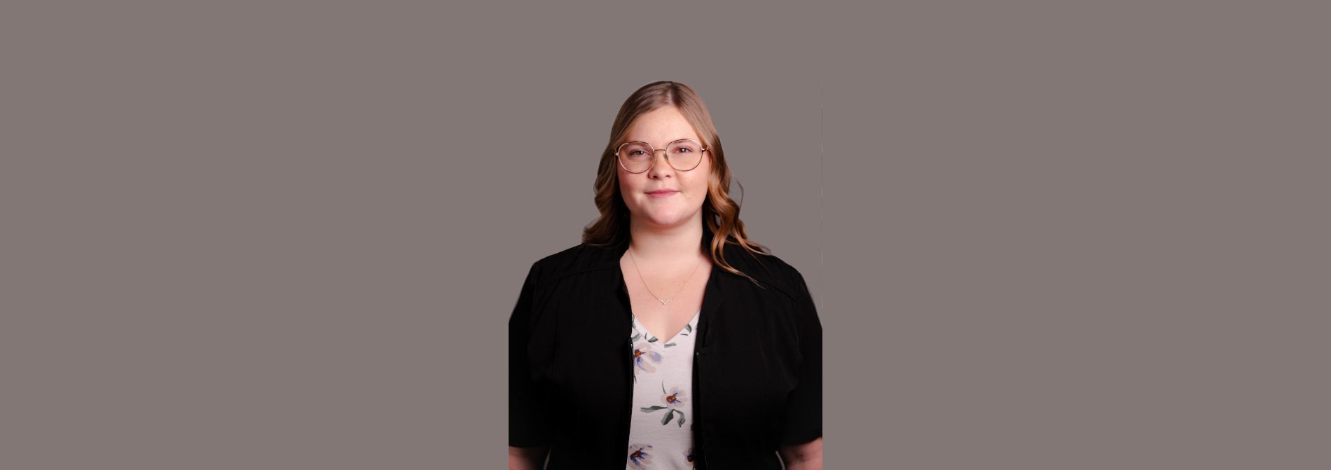 Portrait of a woman with glasses, wearing a black cardigan over a floral blouse, looking at the camera.